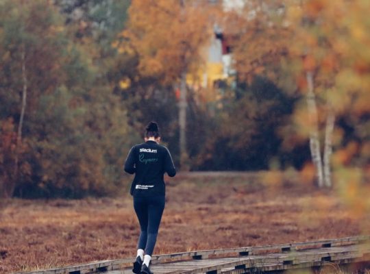 Person jogging on a wooden path surrounded by vibrant autumn foliage in Jönköping, Sweden.